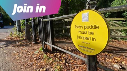 Yellow plaque on a railing saying "Every puddle must be jumped in".