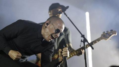 Linkin Park lead singer Chester Bennington screams into a microphone while performing at a live show.