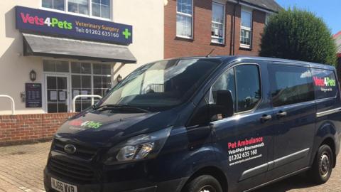 Dark blue van with pet ambulance branding parking outside a vets.