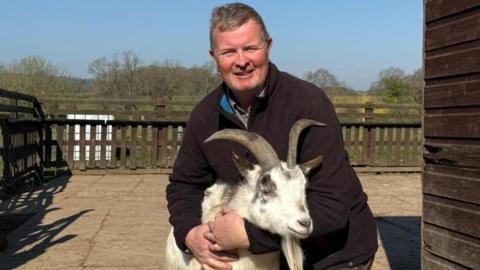 A man cradling a goat inside a farm enclosure
