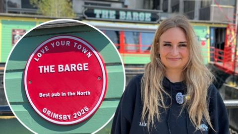 Woman standing in front of a red plaque for The Barge in Grimsby.