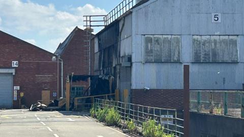 A red brick building covered in metal sheeting has scorch and burn marks across one side. 