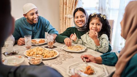 Joyful family gathers around the dining table enjoying a meal and conversation during an Eid dinner at home during Ramadan