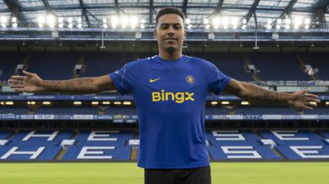 Morgan Rogers stands with his arms outstretched after joining Chelsea