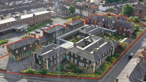 A drone shot of the site with the boundary marked in red. The building is made of old grey brick. The hospital site looks similar to a collection of terraced houses.