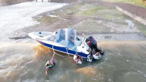 Four men cling to boat as it teeters on edge of dam