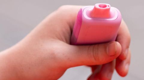 A pink plastic disposable vape being held in someone's hand