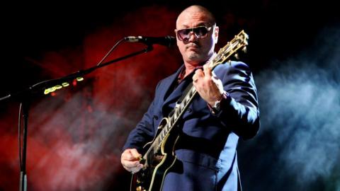 Huey Morgan wearing a navy suit playing an electric guitar