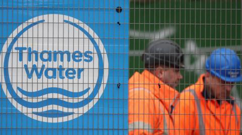 Thames Water workers wearing hard hats behind heras fencing