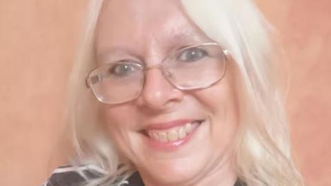 Headshot of Karen Smith against a peach-coloured background. She has long fair hair, glasses and is smiling.
