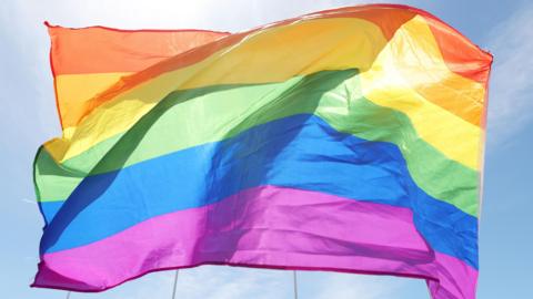 A pride banner flies against a blue sky.