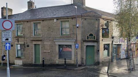 Street view image of the Nag's Head pub. A stone building on a street corner with green windows and doors and a sign in black with gold wording over the door, which is on the corner, that says NAG'S HEAD
