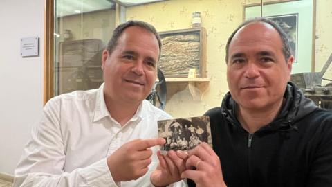 Identical twins Xavier and Joan Carles Lluch looking at an old photograph of their grandfather. Both have short dark hair and identical facial features