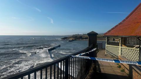 Police tape is fastened to metal railings overlooking Cullercoats Bay.