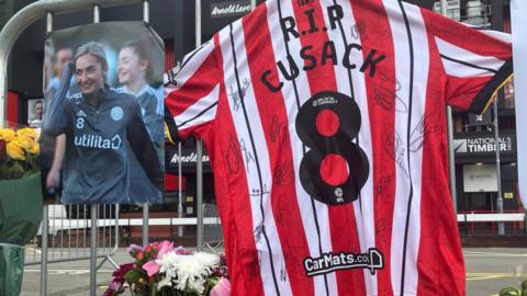 Railings with a photograph of Maddy Cusack, a signed Sheffield United shirt with the number eight and flowers