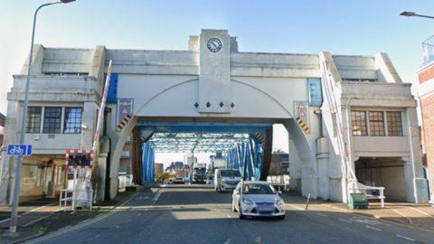 Cars are driving under the bridge towards the camera. The sky is blue.