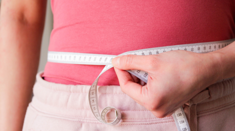 A woman in a pink top with a tape measure around her waist