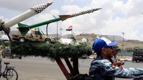 Houthi militiaman rides in front of sculpture of missiles
