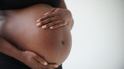 A stock photo of the midsection of a pregnant woman holding her belly.