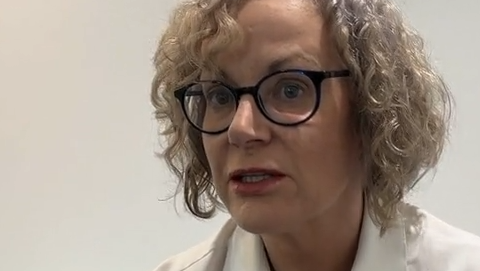 Jersey's children's commissioner Dr Carmel Corrigan. She has curly grey and blonde hair. She is wearing round black-rimmed glasses. She has a white blouse on and is sat on a blue sofa.