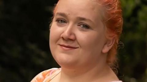 A head and shoulders shot of Rhiannon Whyte wearing a pink and orange dress. Her hair is coloured orange