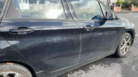 A navy blue car which appears to have been keyed along its driver side doors while parked on a road in Exeter.