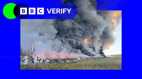 A BBC Verify graphic next to an image of a huge plume of smoke rising from the remains of a building.