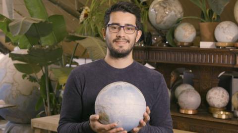 A man holding a globe with more globes in the background.