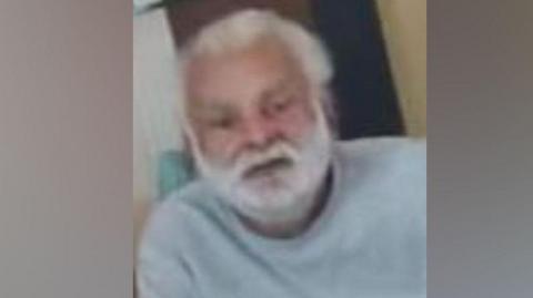 Sukhjinder Singh-Gill: A man with white hair and and white beard wearing a pale grey, round-necked. long-sleeved, top.