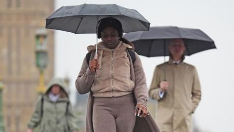 A woman and a man walk down Westminster Bridge in London holding umbrellas on Friday.