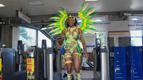 A woman in green and yellow carnival costume arriving at Westbourne Park underground station ahead of the parade.