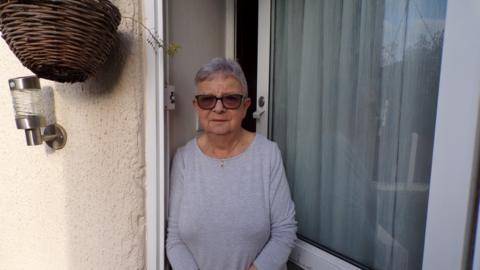 Woman wearing a grey top standing by her front door