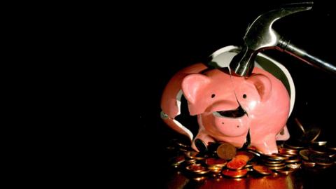 A piggy bank being broken by a hammer as money falls out.