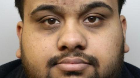 A police-issued photograph of Ahmed, he has short dark hair and a shor beard. He wears a black T-shirt.