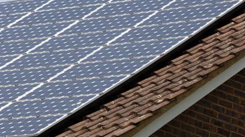 Close-up of a sloped house roof fitted with rows of blue solar panels mounted above brown tiled roofing.