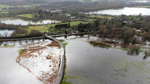 An aerial image shows a flooded road surrounded by standing water in a rural setting with trees, greenery and more floodwater in the background, in Hampshire on Friday.