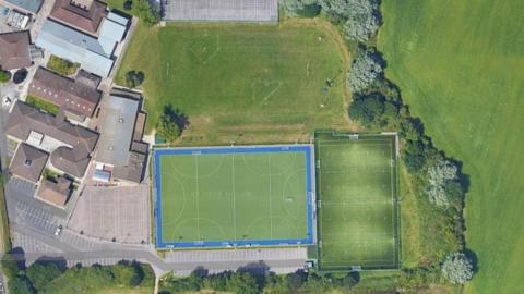 An aerial view of the football pitch at St Peter's High School. The school is on the left, with three pitches next to each other in the middle and a large field beside the bordering hedge on the right.