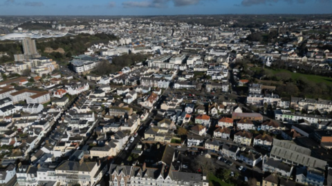 An ariel view of St Helier in Jersey. Dozens of rows of houses are visible under a blue sky.