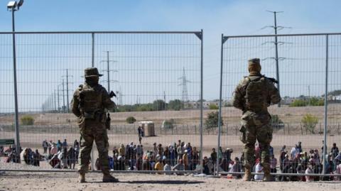 US soldiers watch over a group of migrants waiting to be allowed by the authorities to go to a CBP processing centre in El Paso