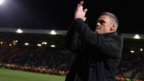 Bradford City boss Graham Alexander, who is wearing a black coat, applauds the fans at Valley Parade.