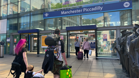 A family walks towards the entrance to a train station bearing the words 'Manchester Piccadilly'.