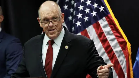 Homan speaking at a news conference in front of a US flag 
