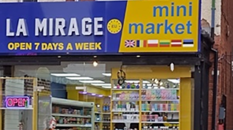 The front of a shop with products on display in the window and the words La Mirage Mini Market on a blue and yellow sign