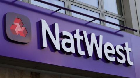 The NatWest branding. It is a purple sign with white writing and a black square with three red cubes in it. 