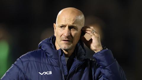 Newcastle Red Bulls head coach Alan Dickens holding an earpiece in his left ear during his team's match with Sale Sharks