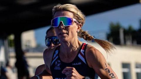 Zoe Tucker competing with a blue GBR running vest, the number 1720 on her arm, and a stadium of spectators behind her.