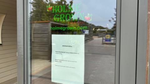 The front window of the building showing a glass door. It has the green logo for Holme Grown and a signing saying the company had ceased trading.