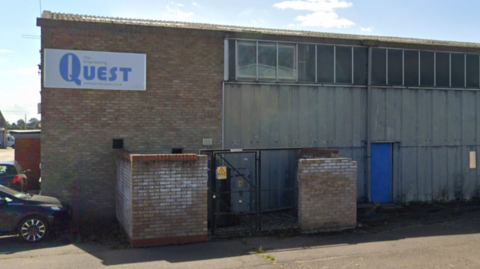 The exterior of a small industrial unit made of brick and metal panelling. It has a sign that says "The Engineering QUEST" on it