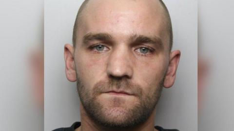 A police custody image of a man with large ears and a close shaven beard.