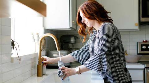 Woman stands at running kitchen tap and fills up water bottle